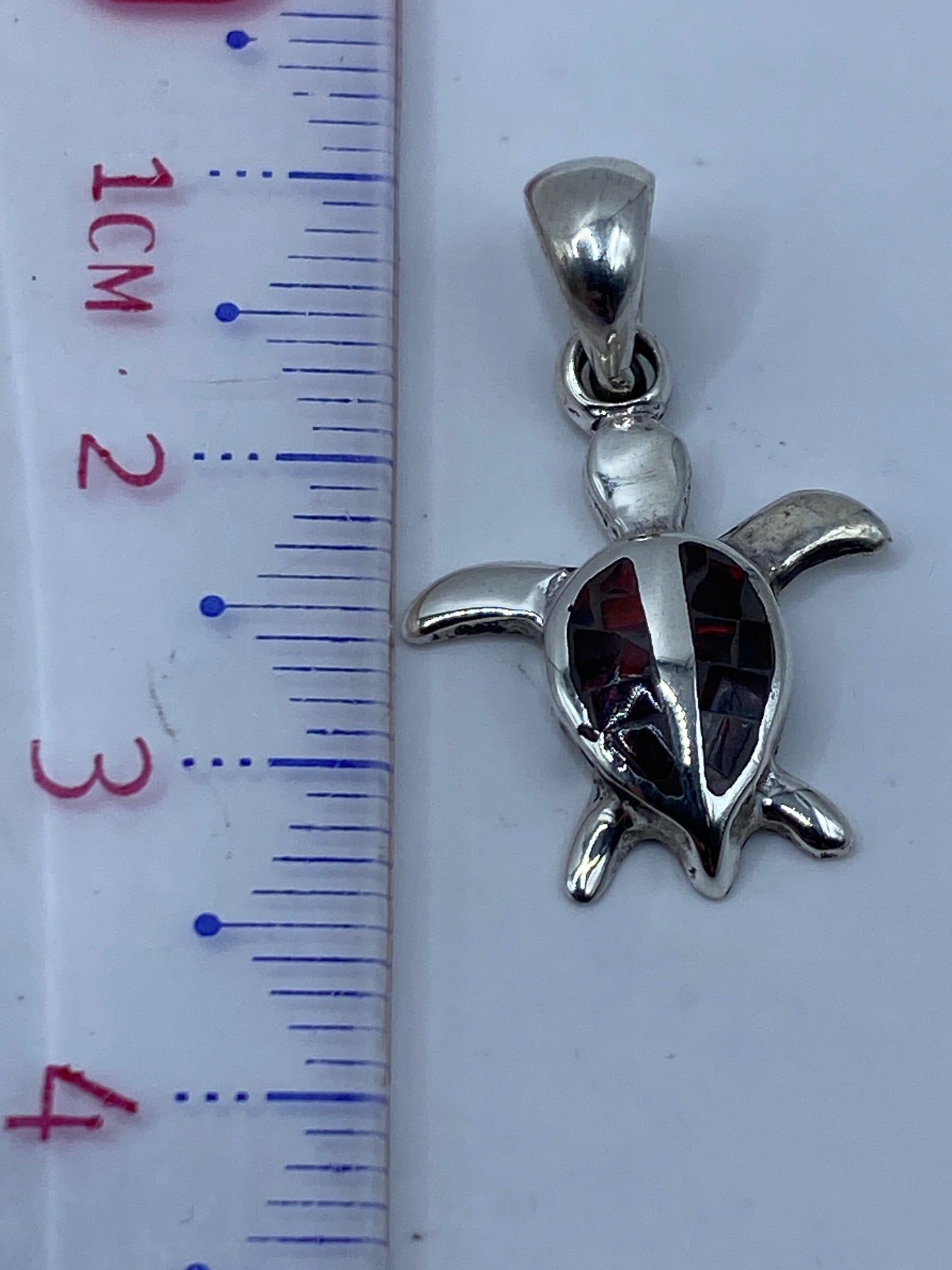 Dije de tortuga sobre escala en centímetros (3.2 cm de largo) junto a marcas de peso en gramos