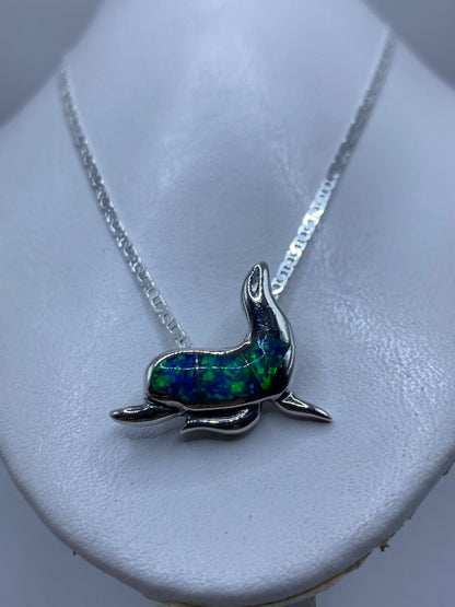 Dije de delfín puesto al cuello sobre piel, efecto del ópalo reflejando luz azul verdosa