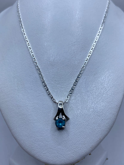 Dije sobre cadena plateada, llevado al cuello en una blusa blanca