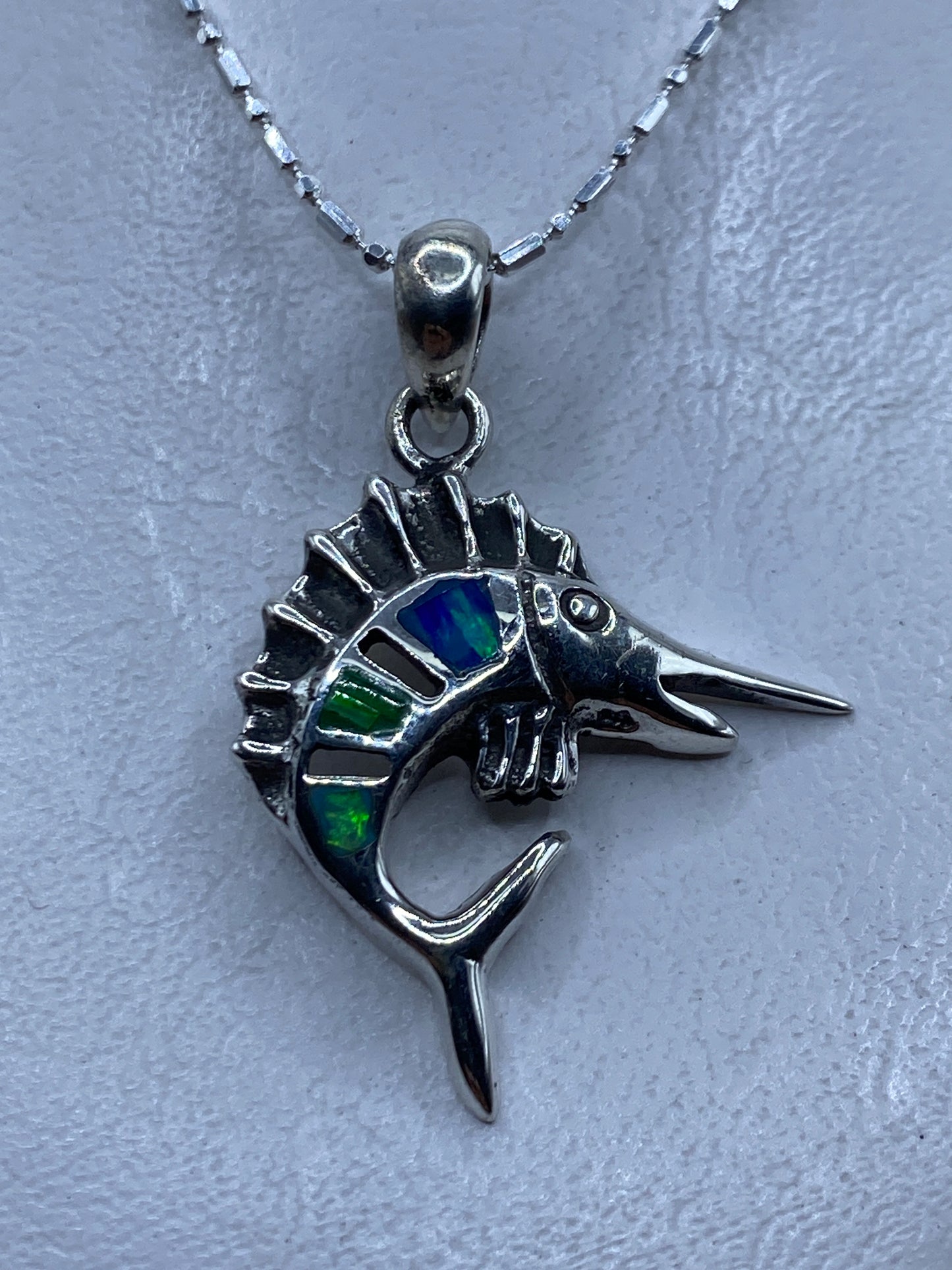 Dije de pez espada en plata .950 con ópalo de fuego multicolor, mostrado en el pecho sobre cadena