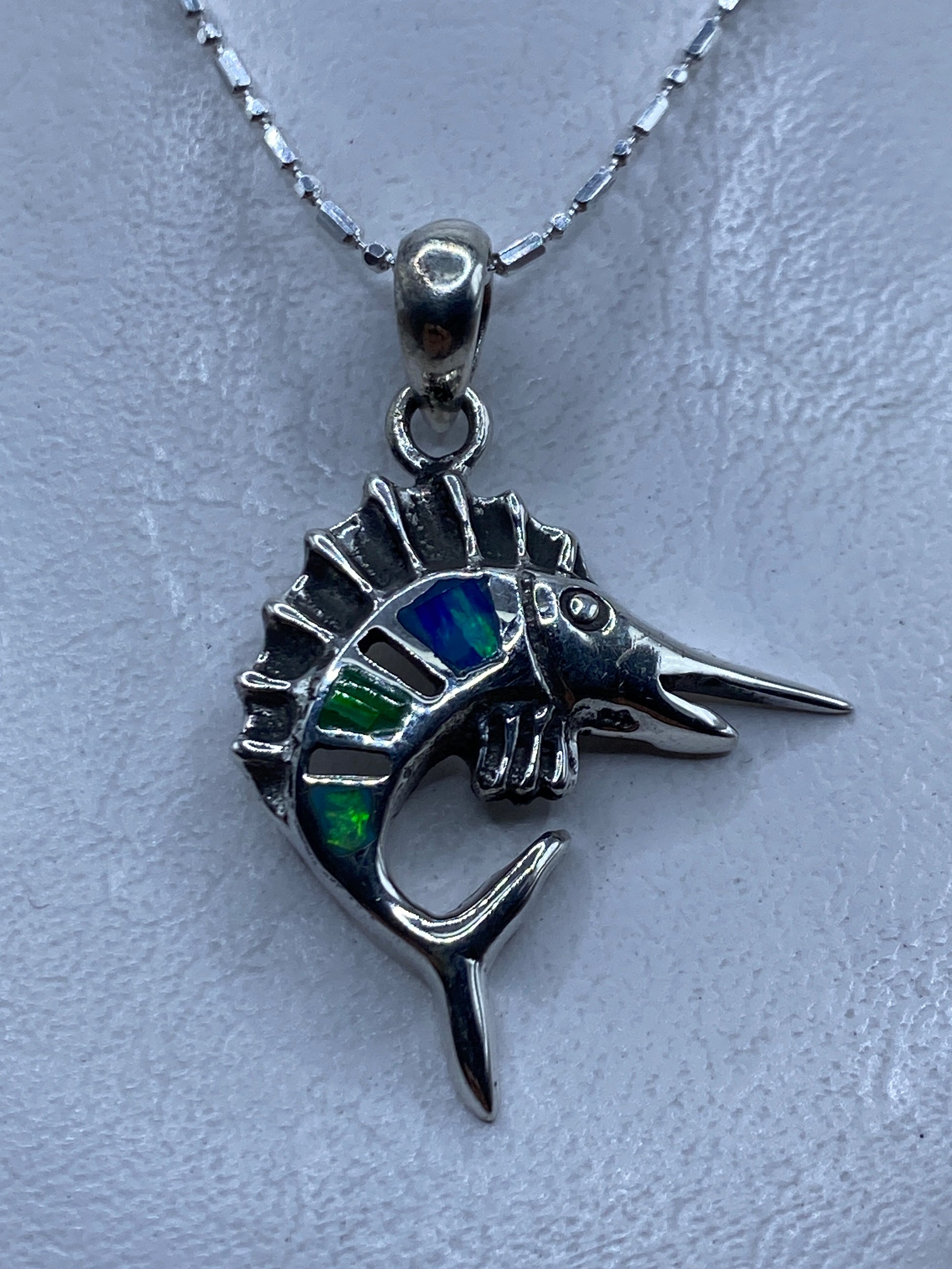 Dije de pez espada en plata .950 con ópalo de fuego multicolor, mostrado en el pecho sobre cadena