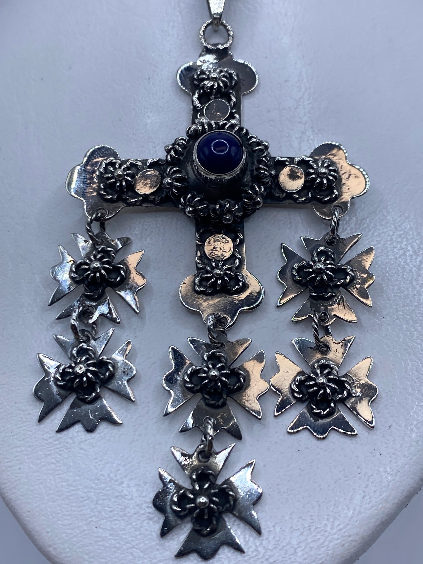 Dije cruz de plata .925 con piedra azul central engastada a mano, colgando de una cadena plateada