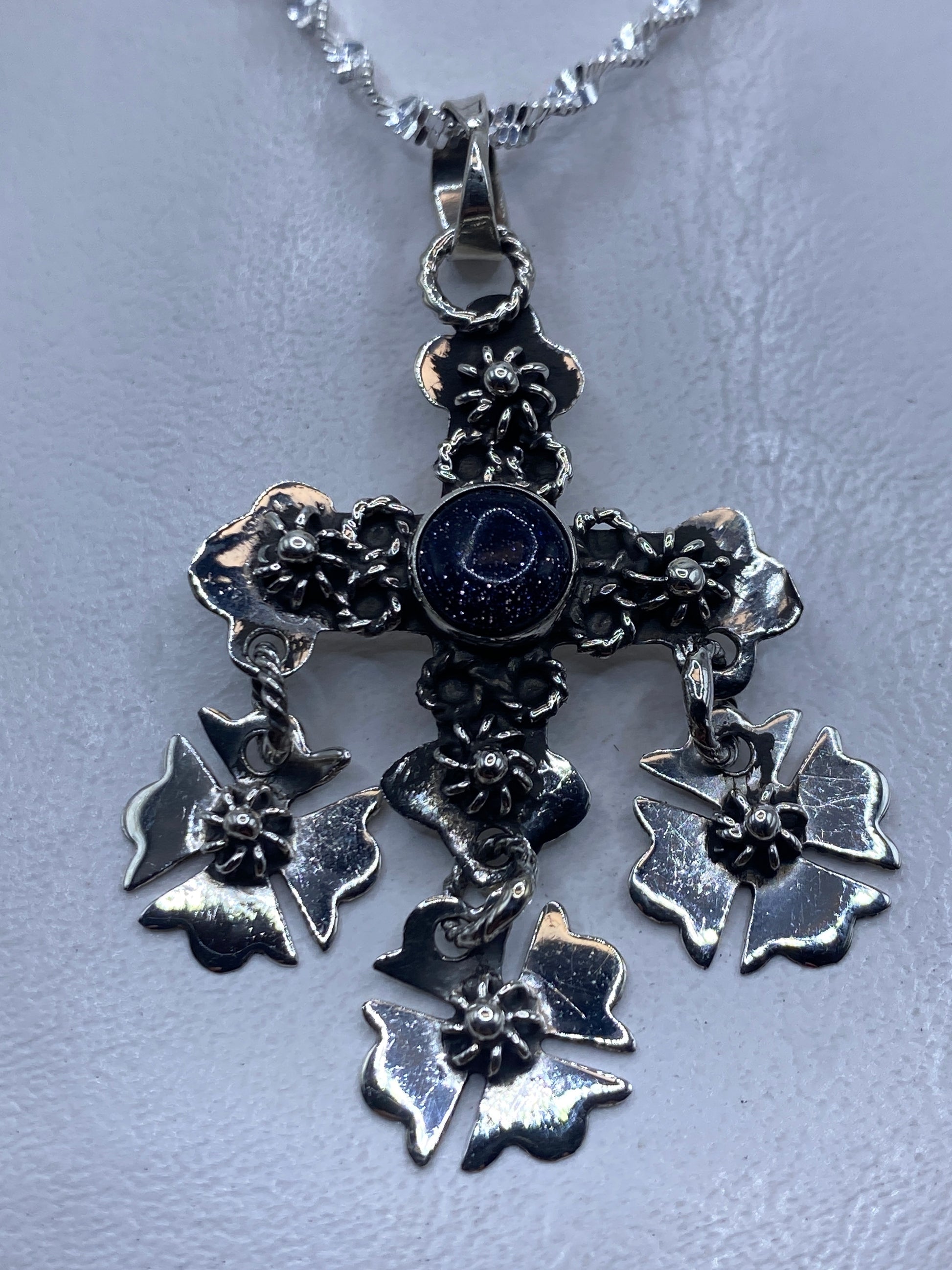 Dije cruz floral de plata .925 con piedra morada colgando en cadena