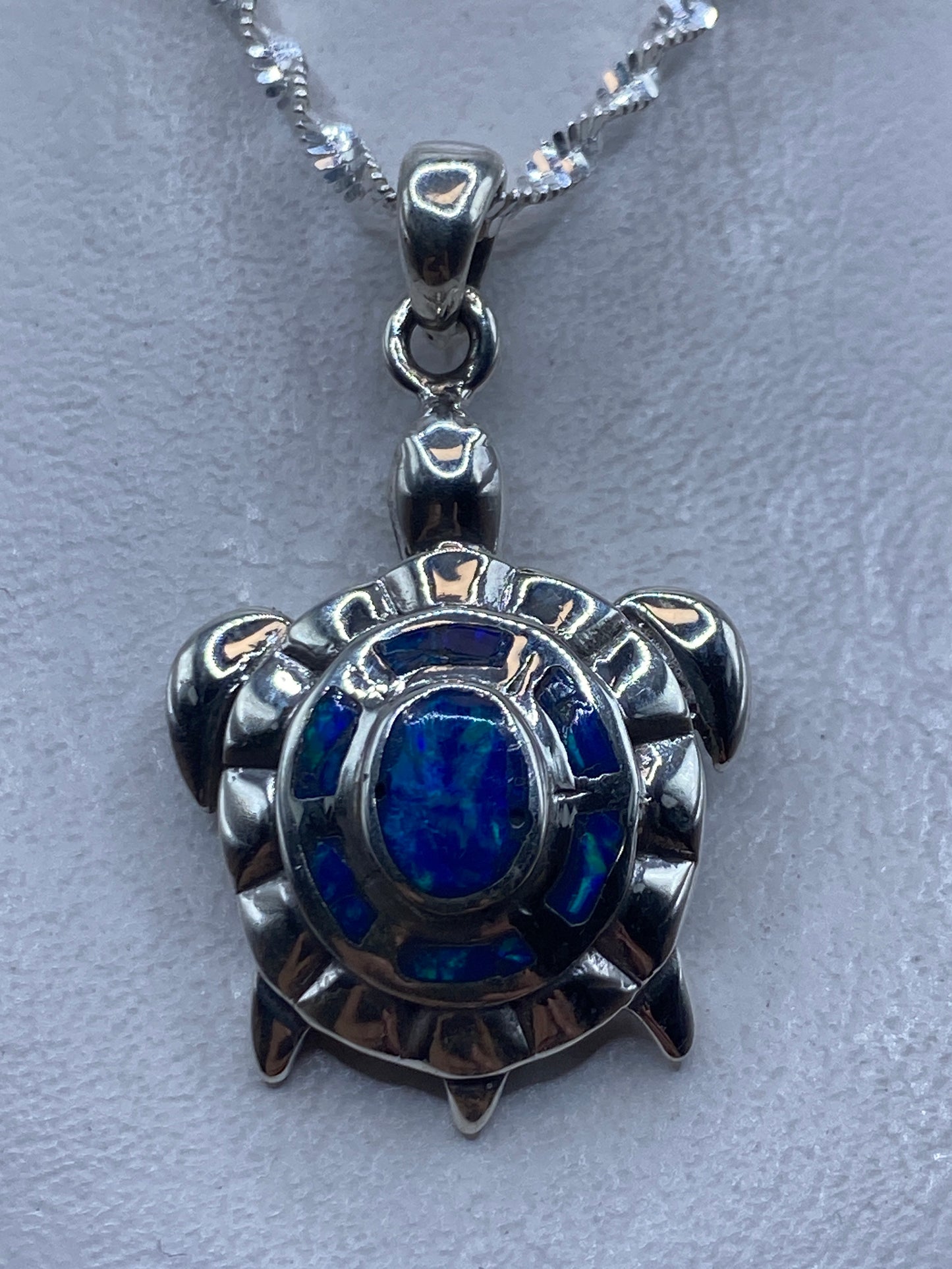 Dije tortuga en plata .950 con Opalo de Fuego azul central, colgando de cadena de plata