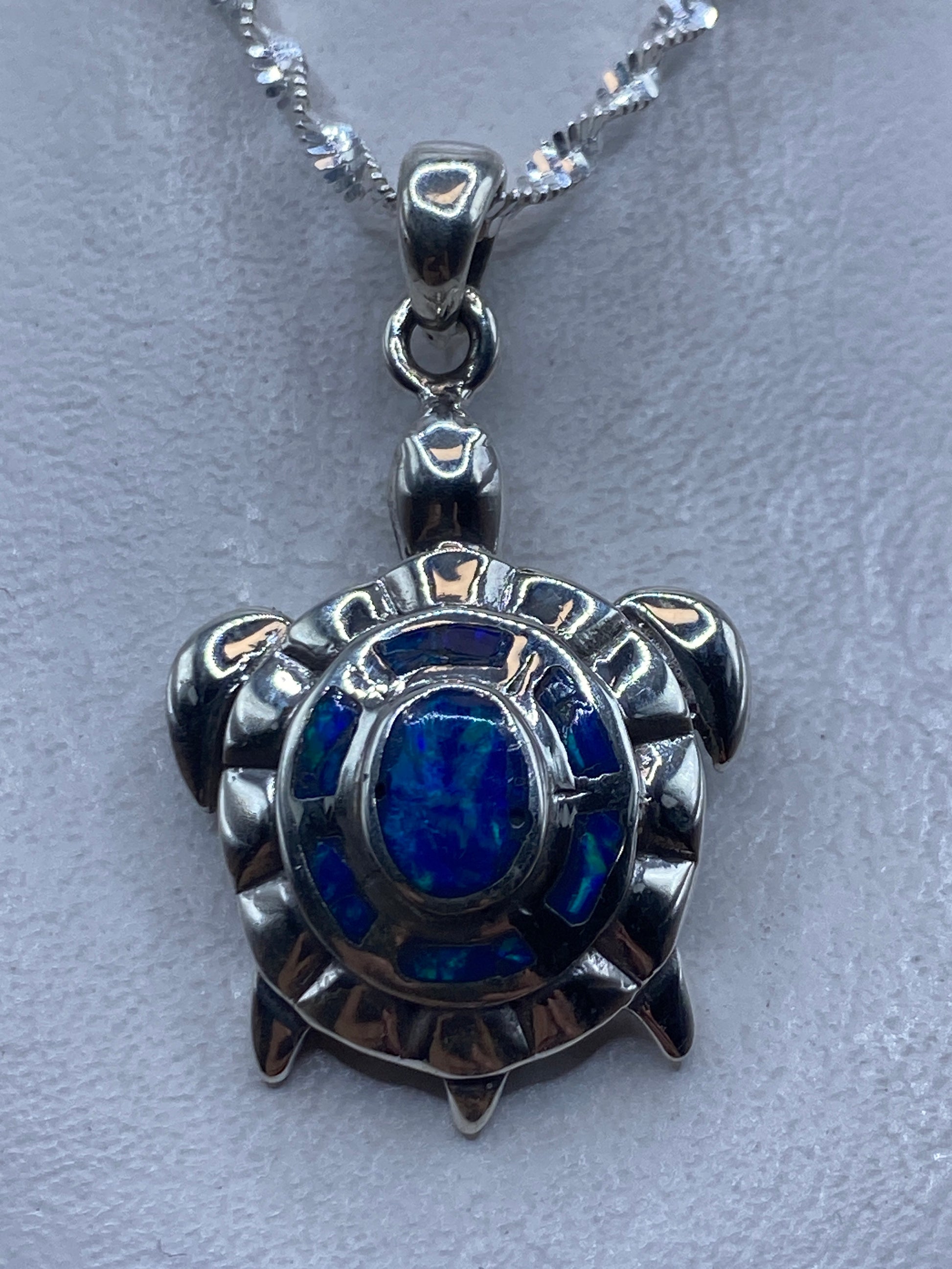 Dije tortuga en plata .950 con Opalo de Fuego azul central, colgando de cadena de plata
