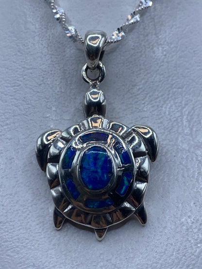 Dije tortuga en plata .950 con Opalo de Fuego azul central, colgando de cadena de plata