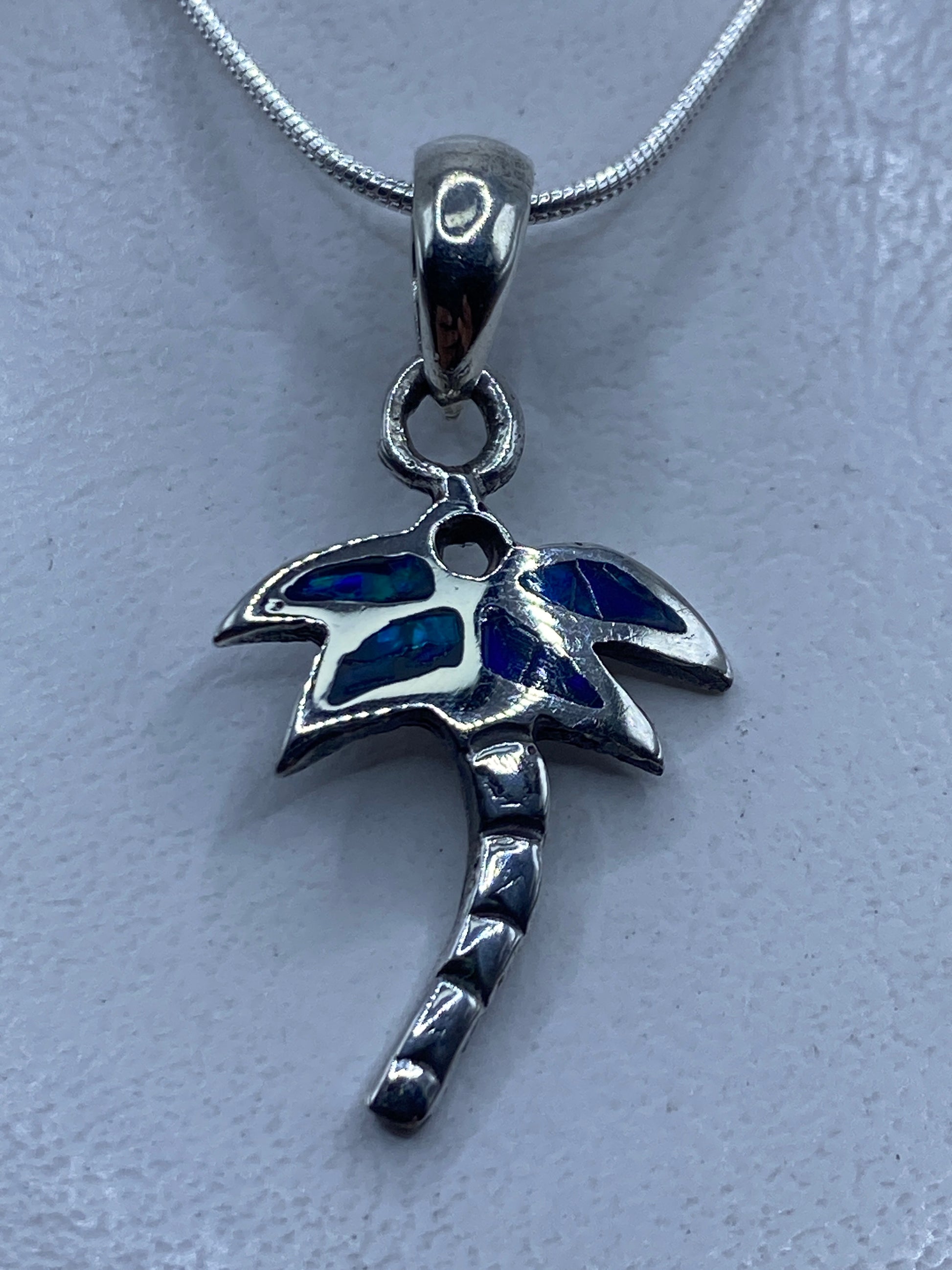 Dije de plata .950 con ópalo de fuego azul engastado a mano, colgando de cadena de plata en el cuello