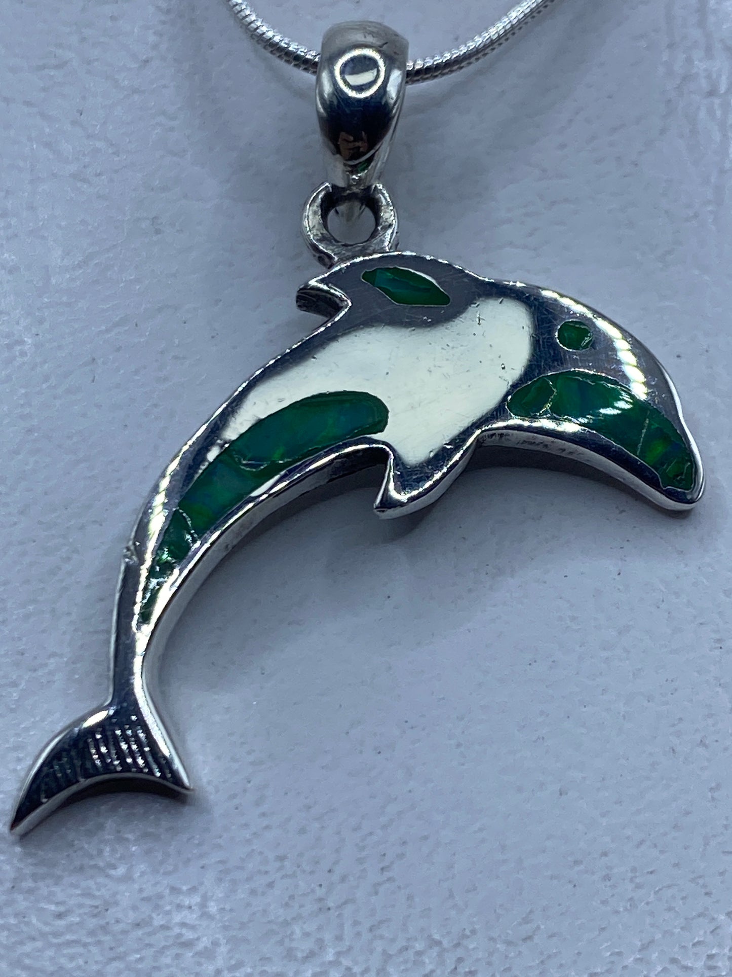 Dije de plata en forma de delfín con ópalo de fuego verde limón engastado, colgando de una cadena de serpentín