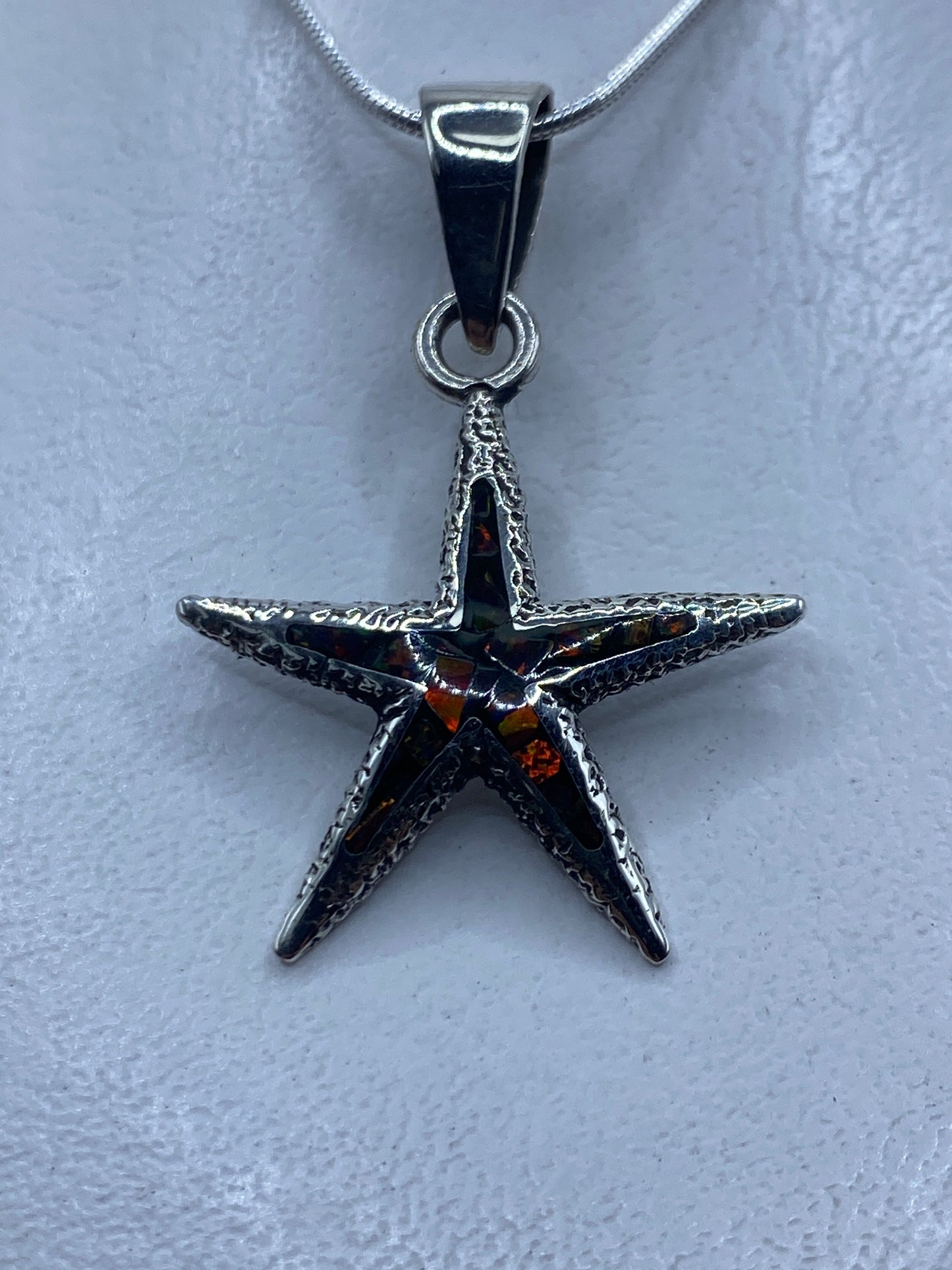 Dije estrella de mar en plata .950 con ópalo de fuego multicolor colgado de cadena plateada