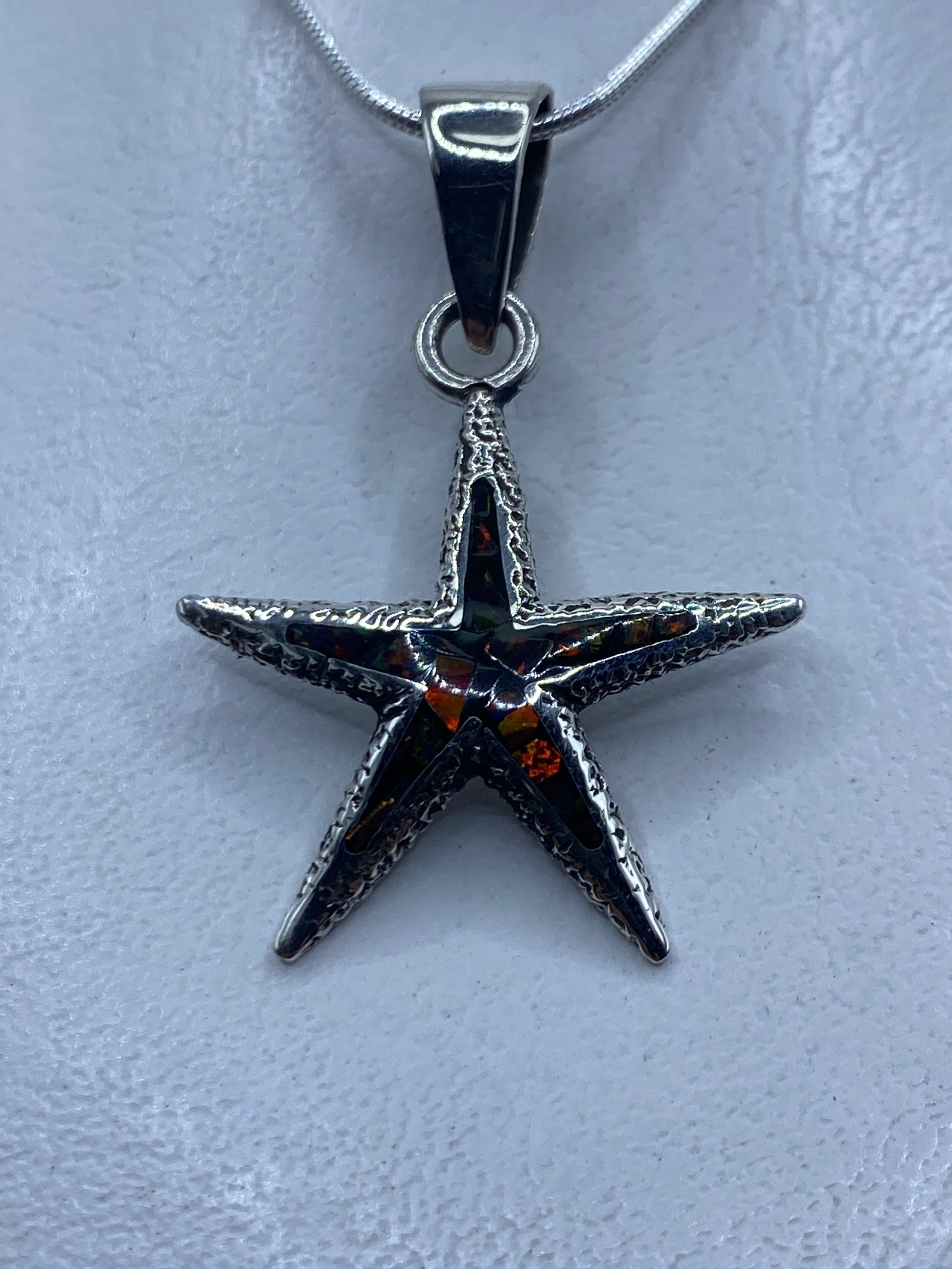 Dije estrella de mar en plata .950 con ópalo de fuego multicolor colgado de cadena plateada