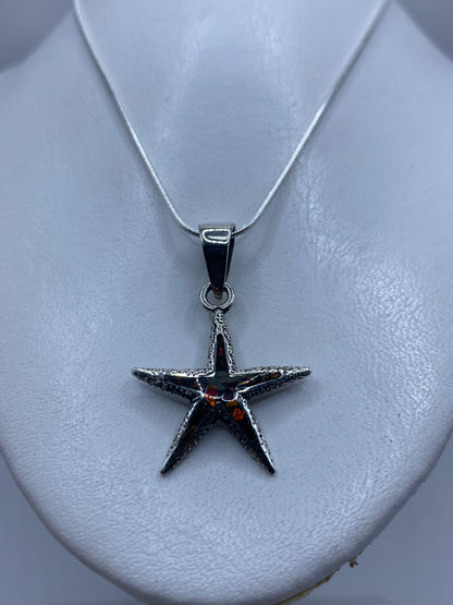 Vista frontal del dije de estrella de mar mostrando el detalle texturizado y el engaste de ópalo