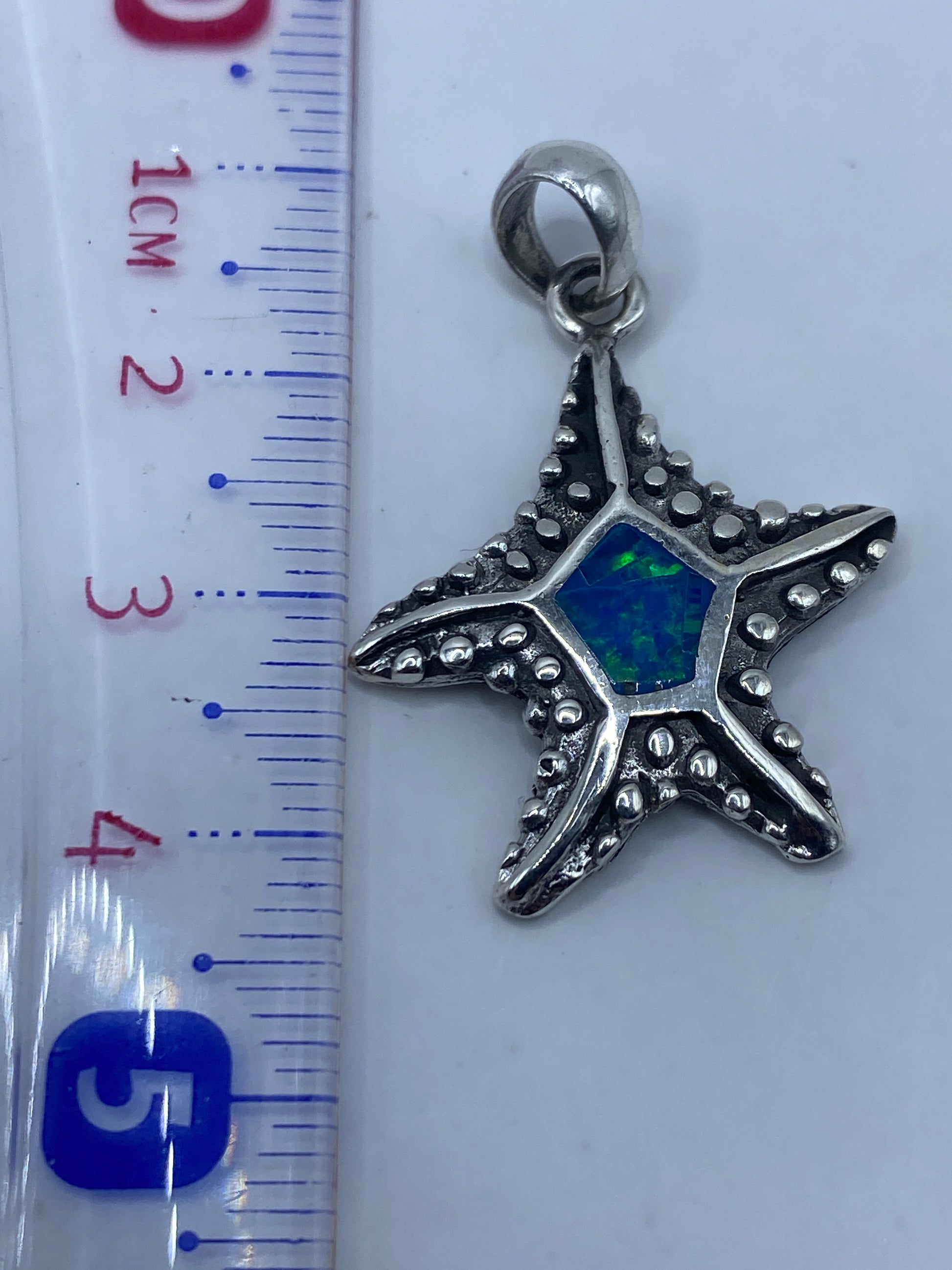 Dije estrella de mar en balanza de precisión junto a regla, 4.2 cm de largo, 3.8 gramos
