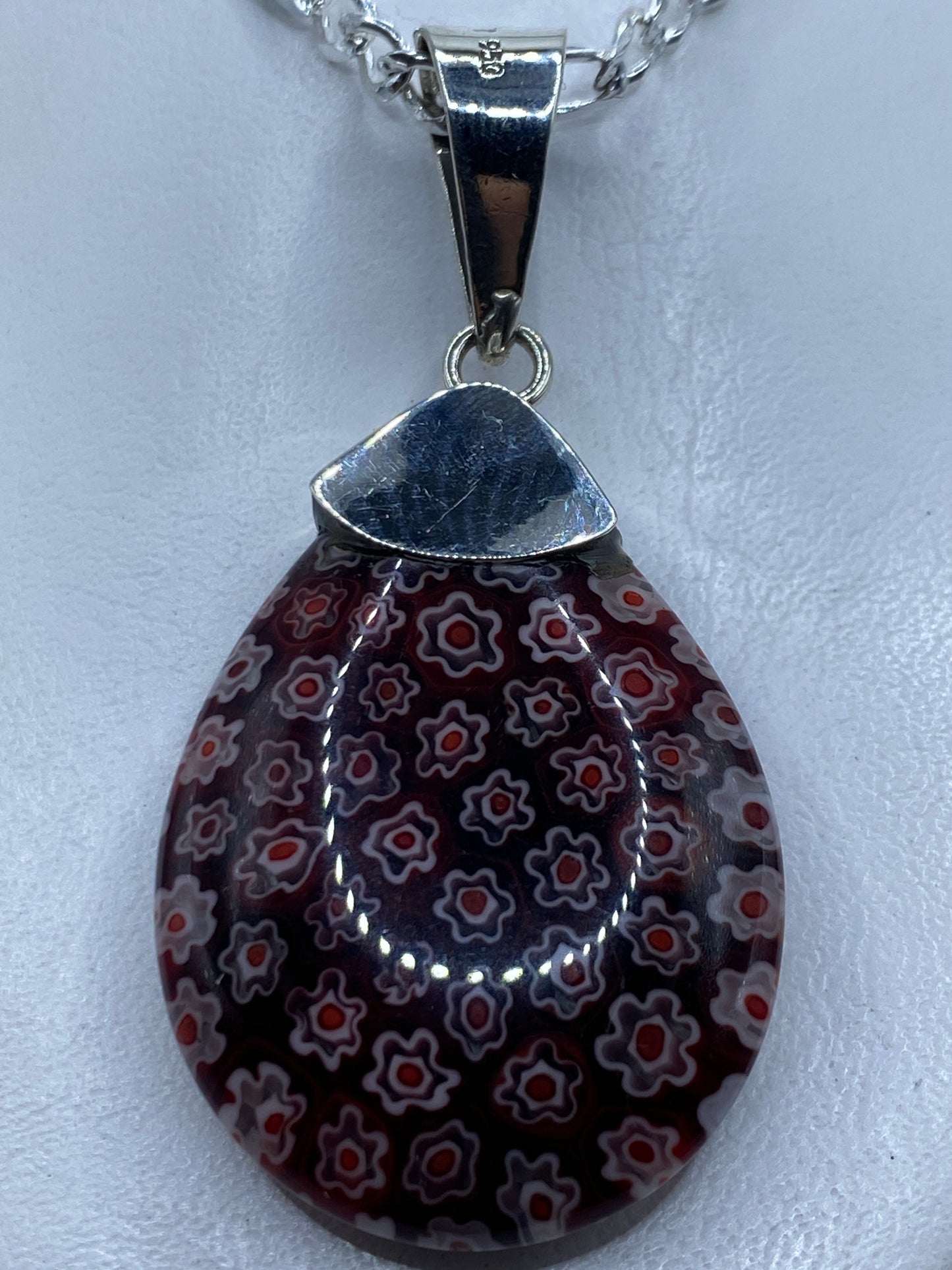 Dije de plata .950 con piedra roja incrustada, colgando de cadena plateada