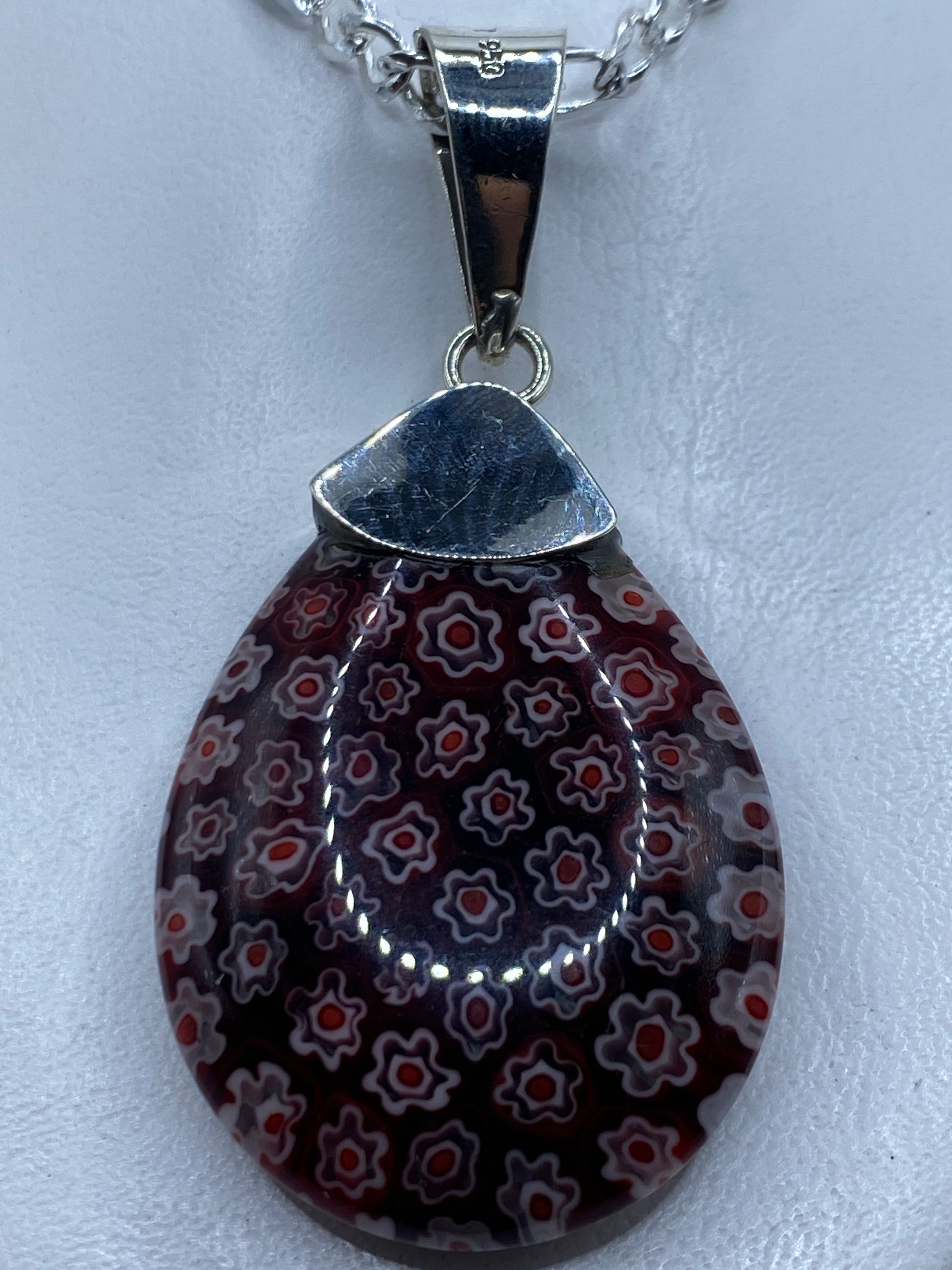 Dije de plata .950 con piedra roja incrustada, colgando de cadena plateada