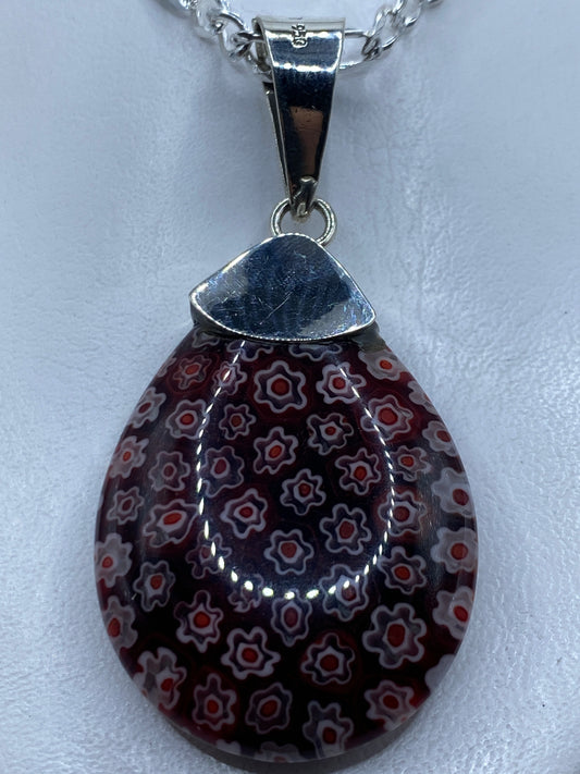Dije de plata .950 con piedra roja incrustada, colgando de cadena plateada