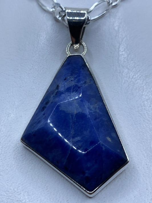 Dije de plata .950 con piedra azul engastada, colgando de cadena de plata en cuello