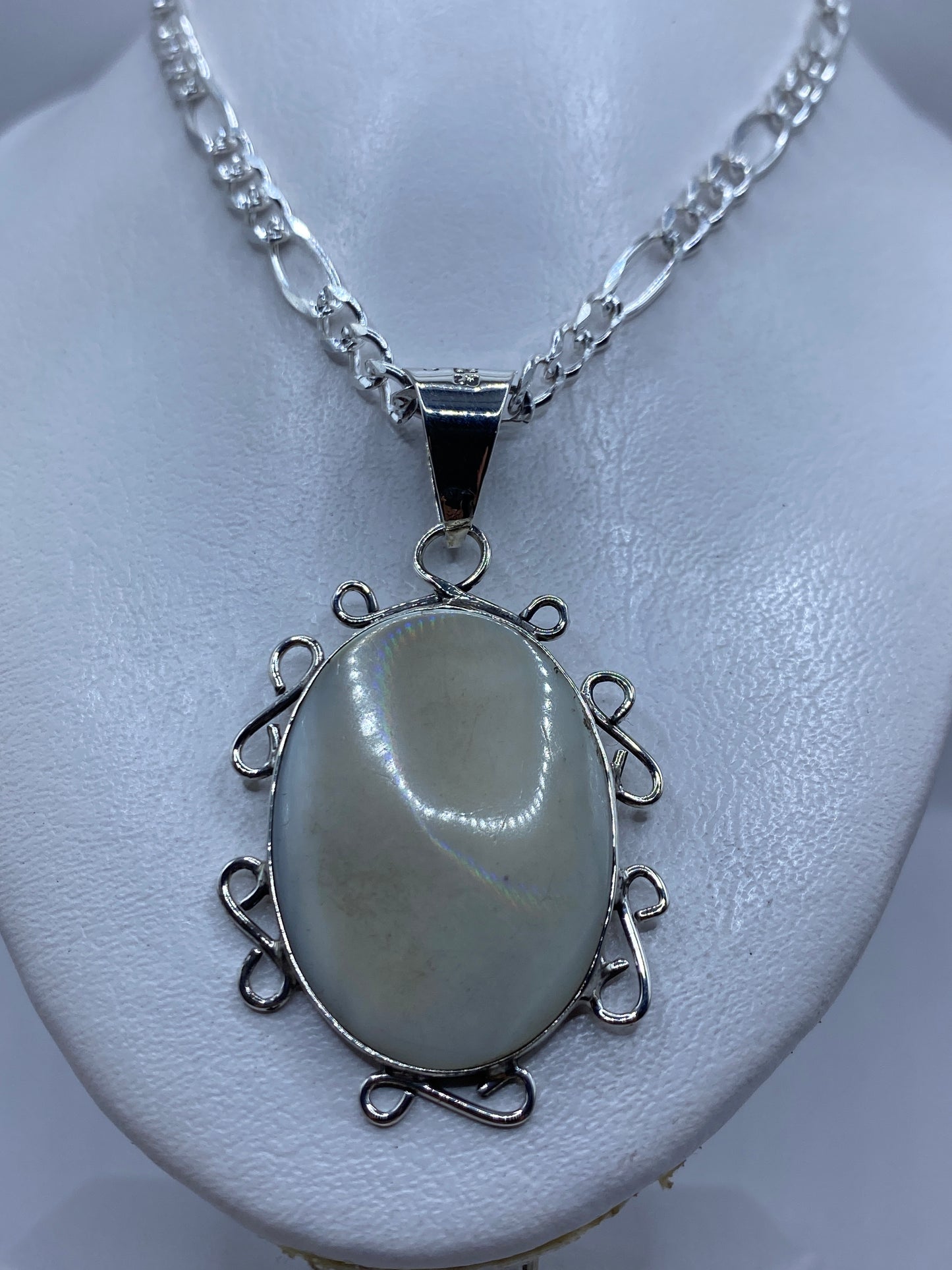 Dije colgando de una cadena de plata figaro, perla blanca nacarada visible