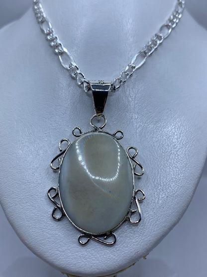 Dije colgando de una cadena de plata figaro, perla blanca nacarada visible