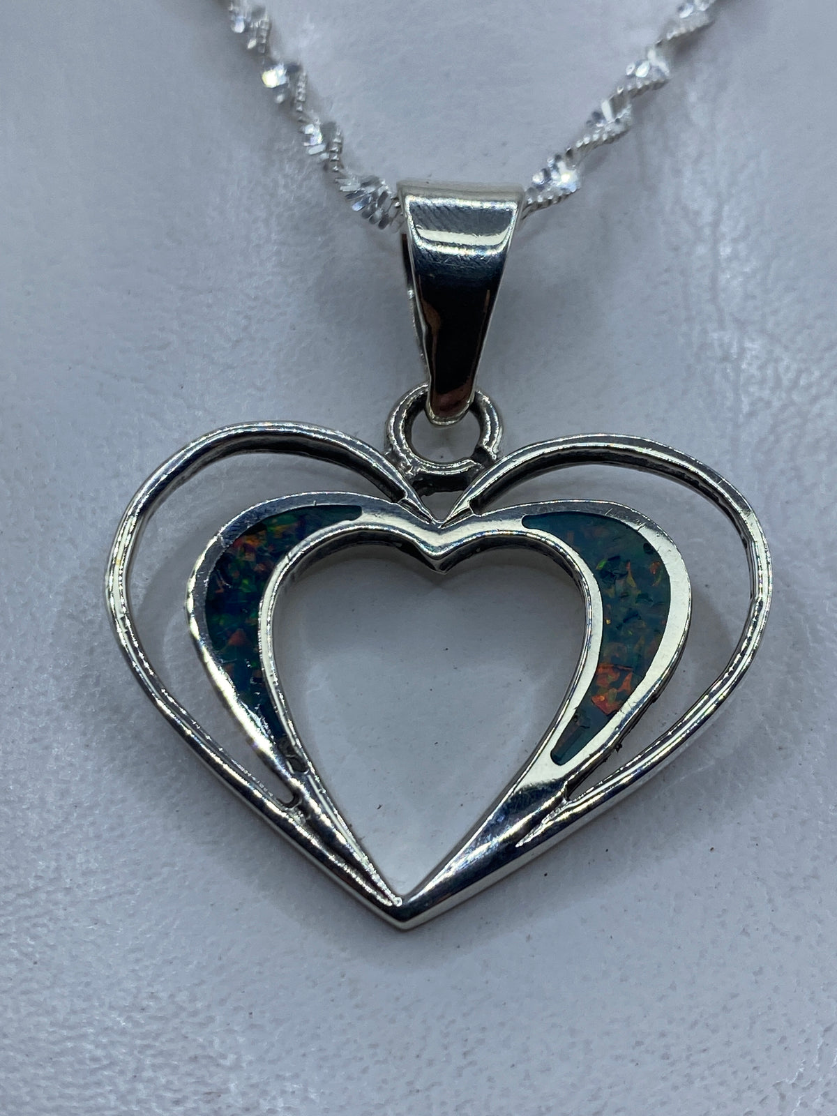 Dije de corazón doble en plata .950 con ópalo de fuego azul, colgado de una cadena plateada