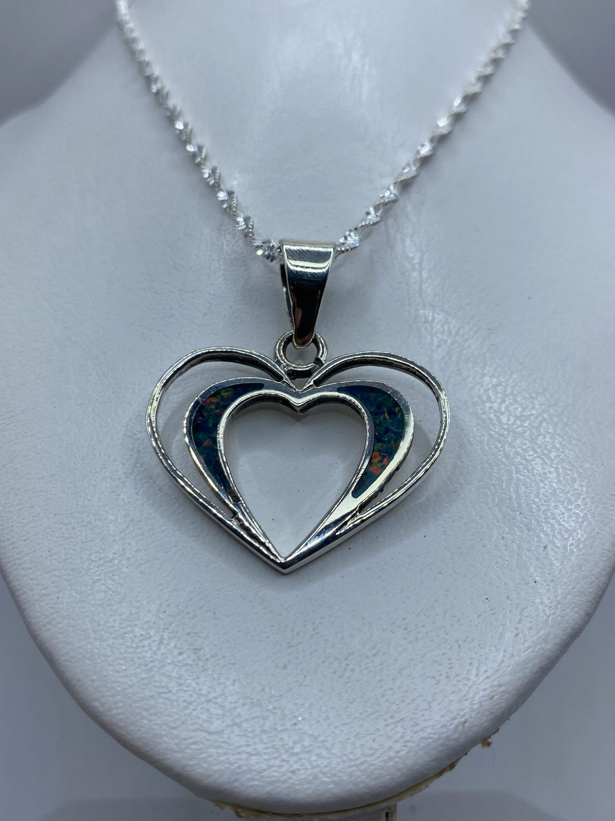 Detalle frontal del dije mostrando la incrustación de ópalo de fuego y el diseño de corazón doble
