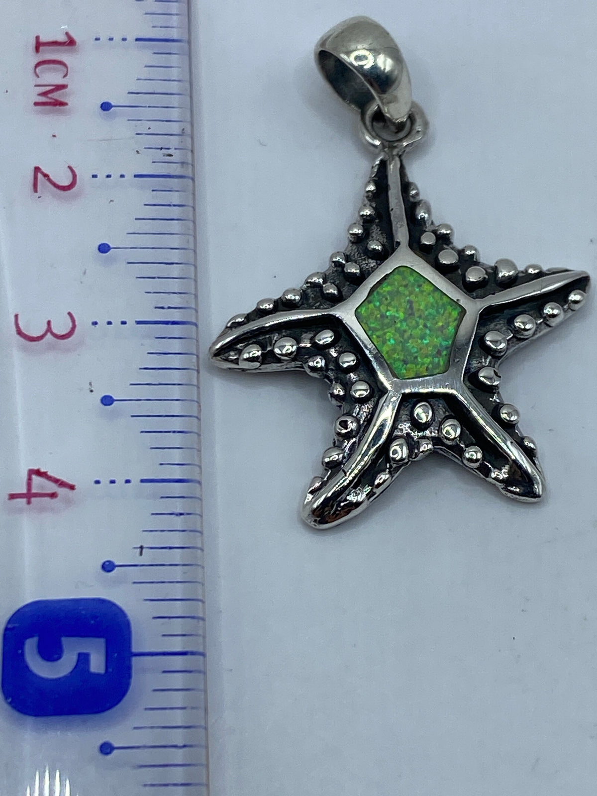 Estrella marina de plata .950 de 4.3 cm junto a regla para escala de tamaño