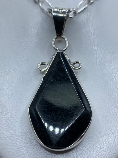 Dije de plata en forma de lágrima con piedra oscura engastada, colgando de cadena de eslabones en el pecho de una mujer