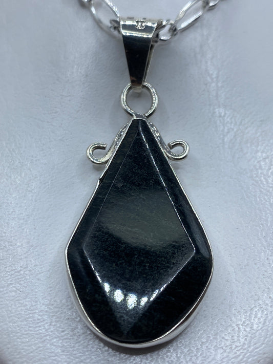 Dije de plata en forma de lágrima con piedra oscura engastada, colgando de cadena de eslabones en el pecho de una mujer