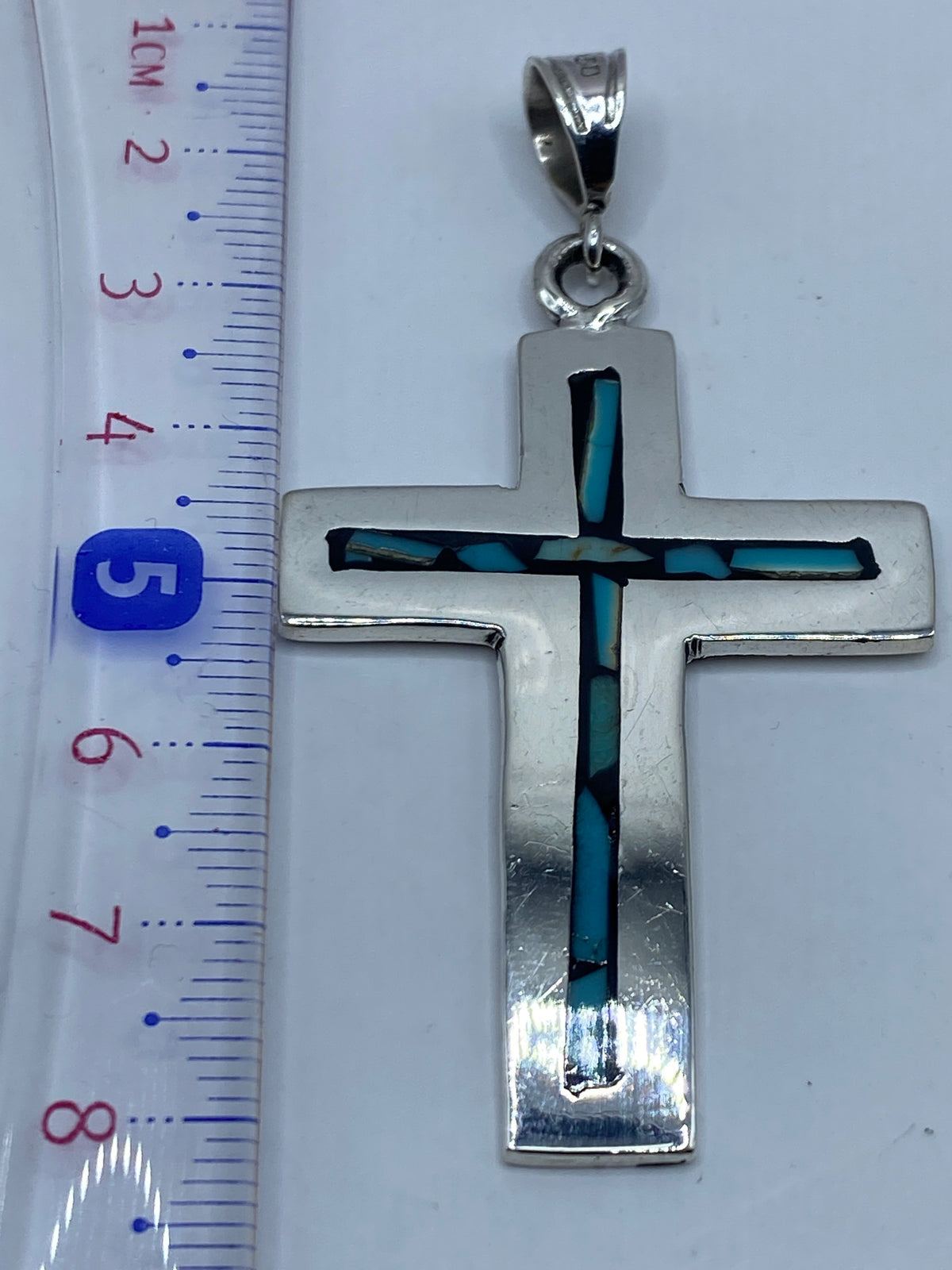 Dije cruz sobre fondo blanco, midiendo 7.6 cm de largo