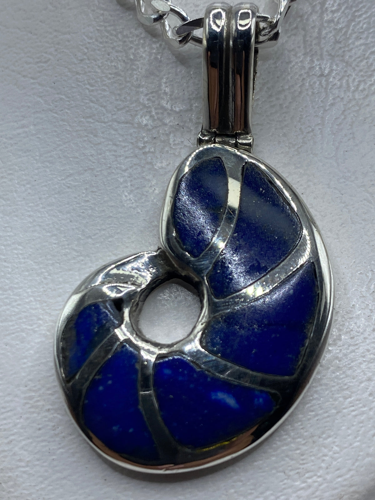 Dije de plata .950 con incrustación de piedra azul, colgado de una cadena figaro