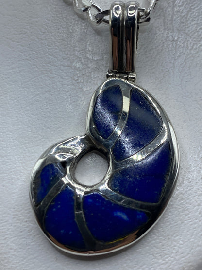 Dije de plata .950 con incrustación de piedra azul, colgado de una cadena figaro