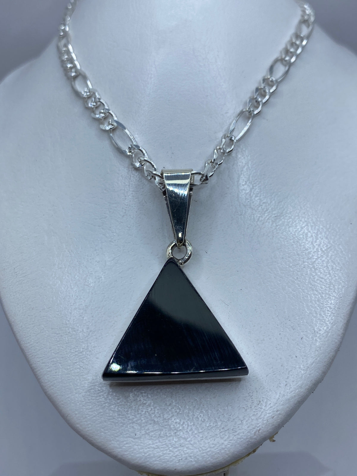 Dije de ónix y plata en la mano, mostrando el tamaño y la geometría pura del triángulo