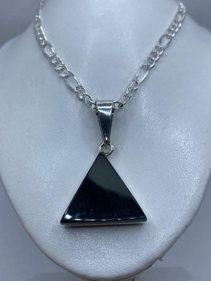 Dije de ónix y plata en la mano, mostrando el tamaño y la geometría pura del triángulo