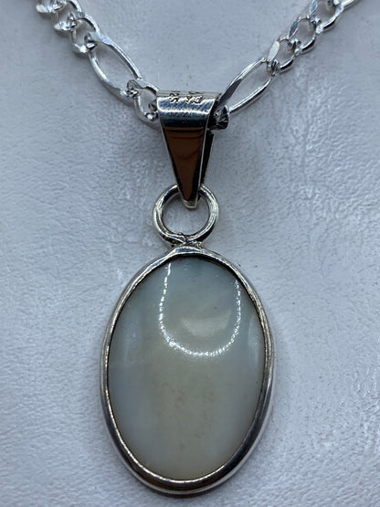 Dije de plata .950 con piedra blanca ovalada engastada, colgando de una cadena figaro