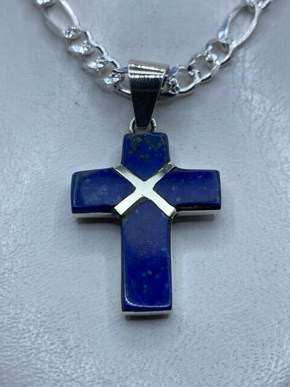 Dije cruz de plata .950 con piedra azul incrustada, colgando de cadena plateada