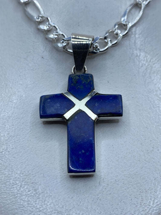 Dije cruz de plata .950 con piedra azul incrustada, colgando de cadena plateada