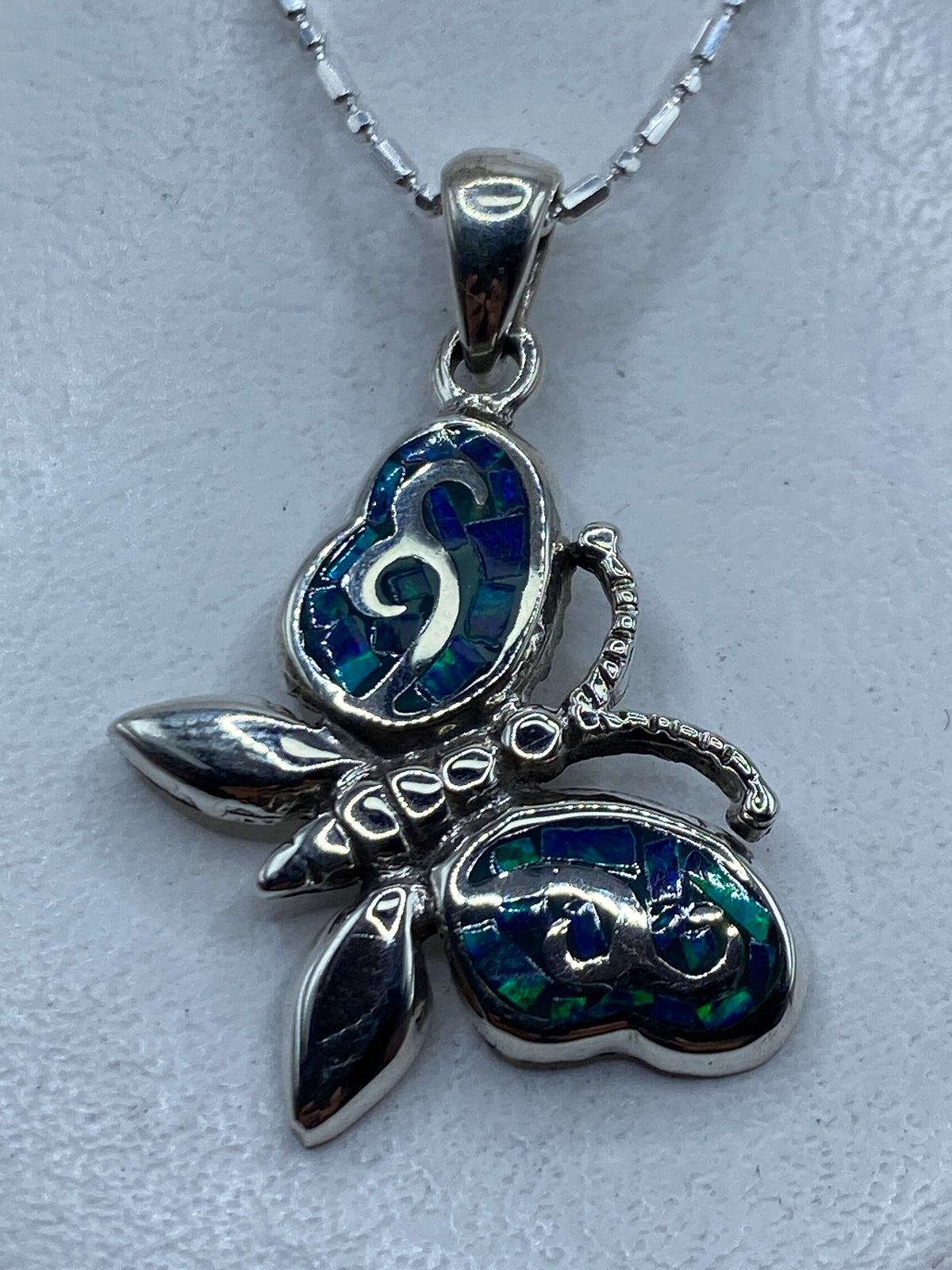 Dije de plata con ópalo de fuego azul incrustado, colgando de una cadena plateada