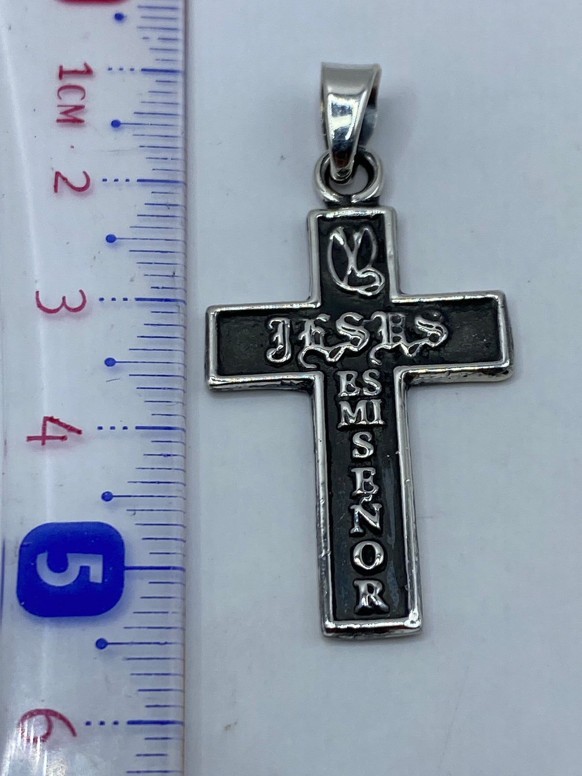 Cruz de plata en la mano, mostrando tamaño real de 5.4 cm