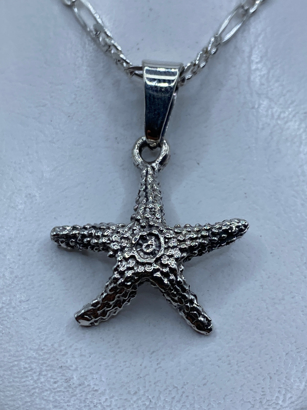 Dije de plata granulado con forma de estrella de mar, colgando de cadena, primer plano detalle