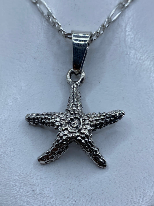 Dije de plata granulado con forma de estrella de mar, colgando de cadena, primer plano detalle