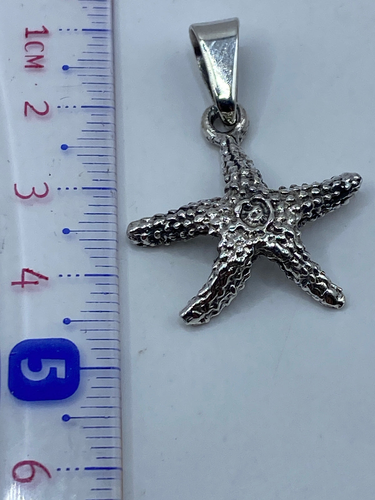 Medida del dije de estrella de mar junto a regla, 4.9 cm de largo