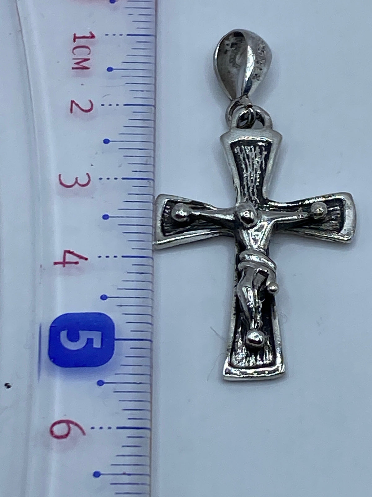 Escala: dije cruz de 5.2 cm al lado de regla métrica