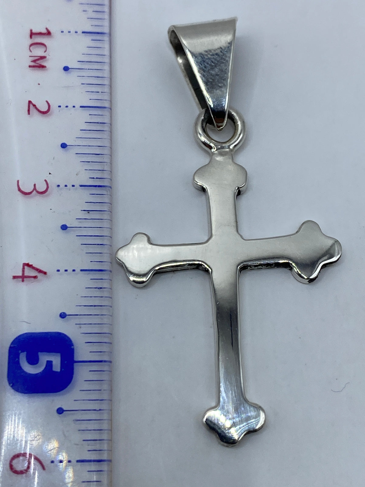 Dije cruz de plata .925 sobre fondo blanco mostrando acabado espejo y peso