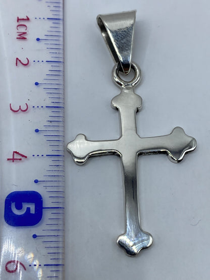 Dije cruz de plata .925 sobre fondo blanco mostrando acabado espejo y peso