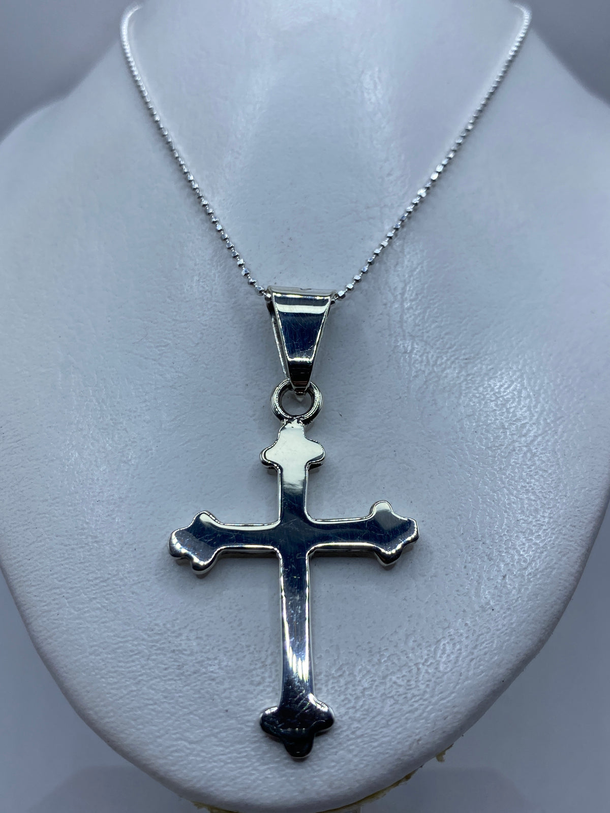 Vista frontal de la cruz religiosa de plata con brazos acampanados y calado delicado