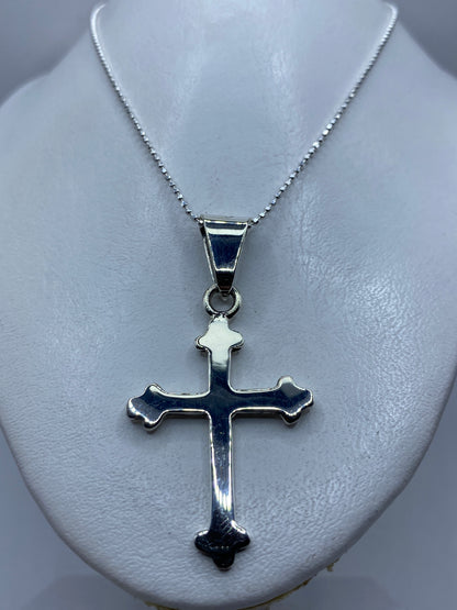 Vista frontal de la cruz religiosa de plata con brazos acampanados y calado delicado