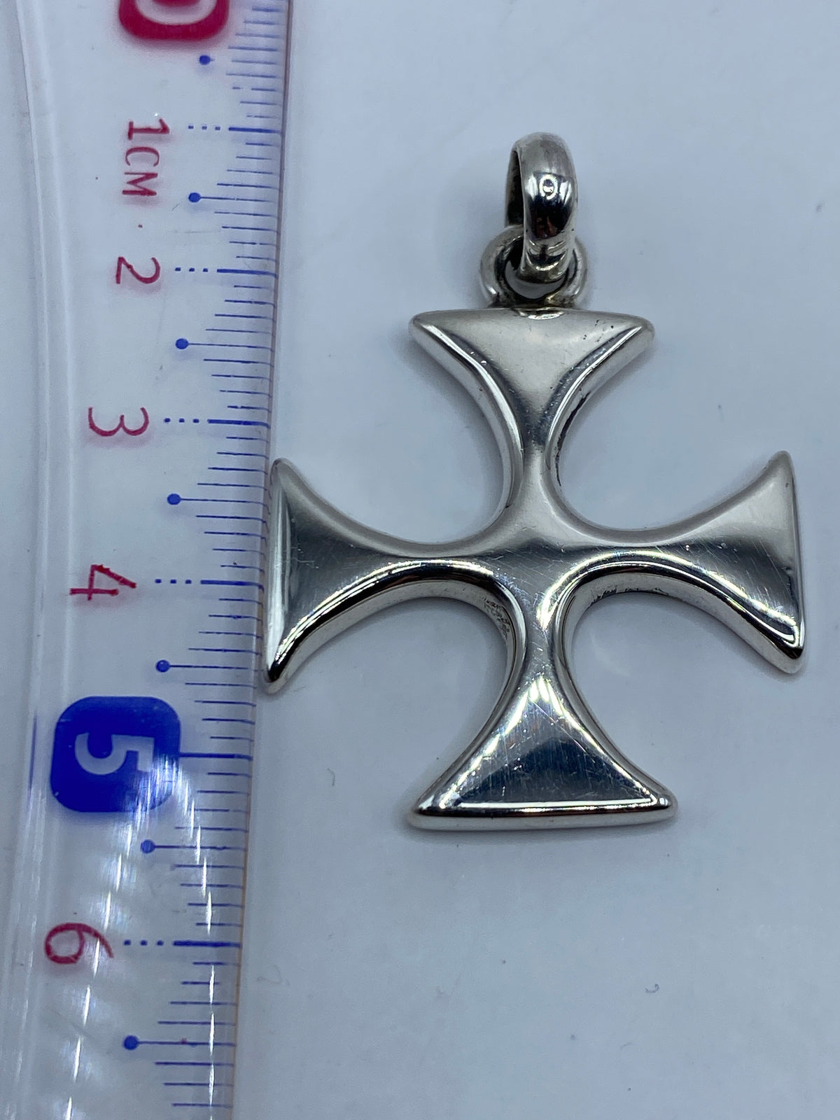 Dije cruz de plata colgado sobre fondo gris para escala de tamaño