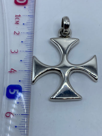 Dije cruz de plata colgado sobre fondo gris para escala de tamaño