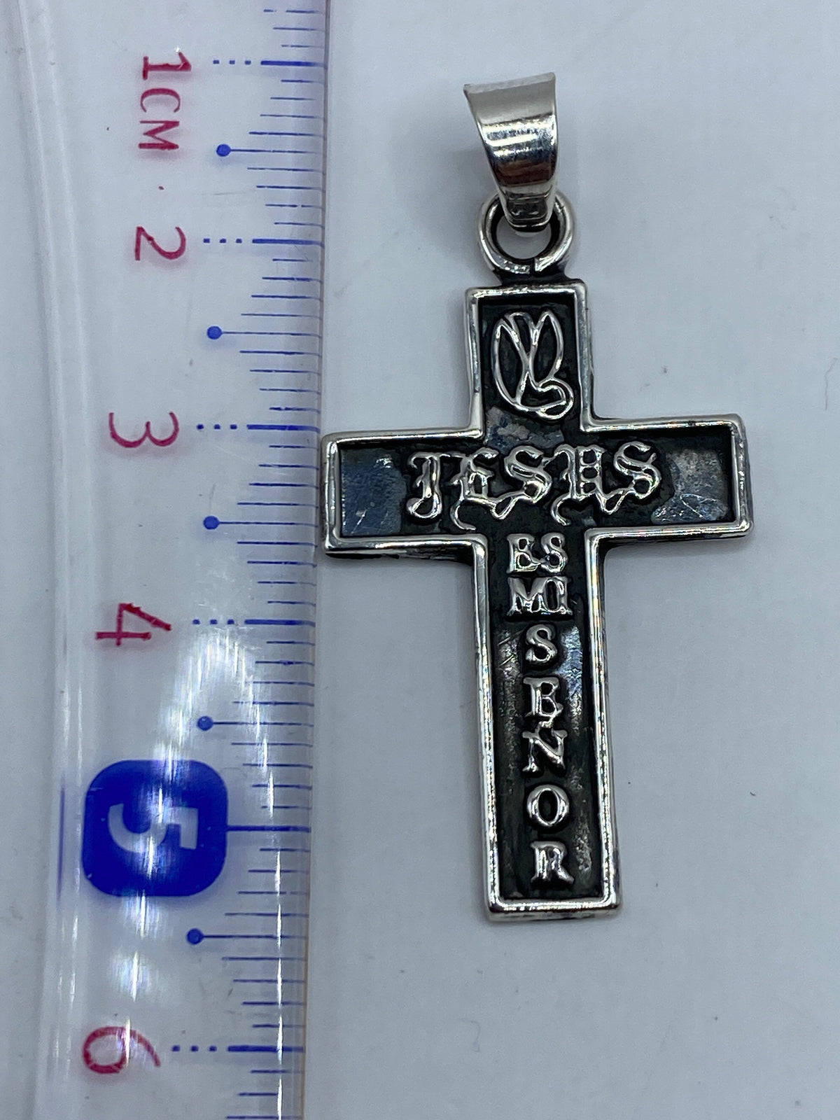 Dije cruz de plata .925 sobre superficie gris mostrando el acabado pulido mate