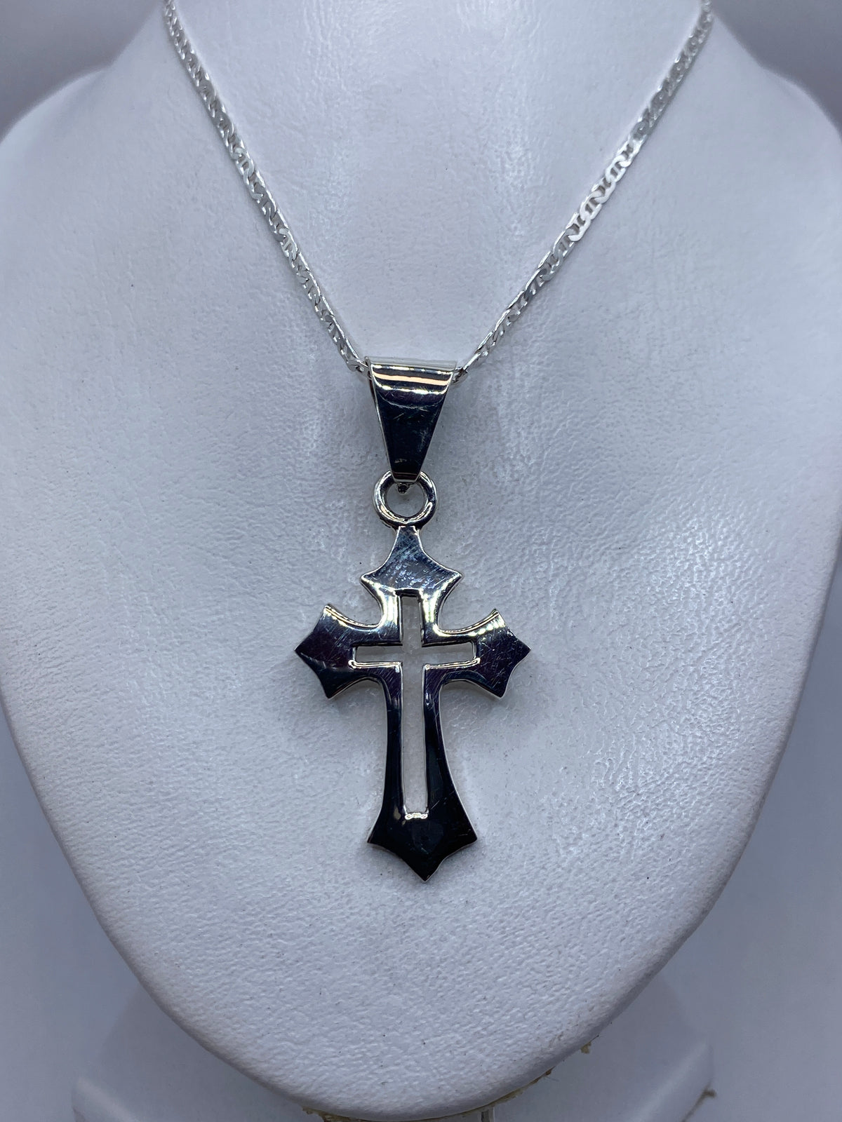 Cruz de plata colgando en cadena plateada, mostrando el diseño cruciforme clásico