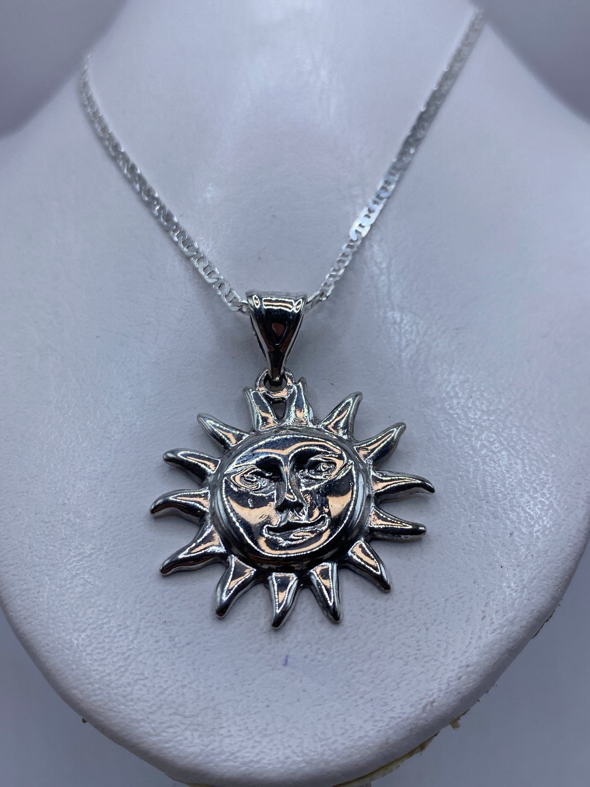 Detalle frontal del dije sol de fundición artesanal con cara antropomórfica y acabado pulido brillante